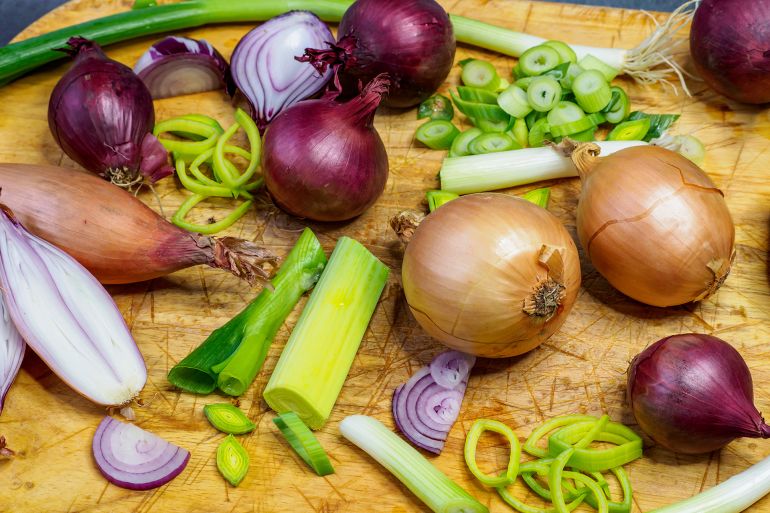 Different types of onion on wooden table. Onions, shallots, red and spring onions variety. by Lubos Chlubny ادوبي ستوك