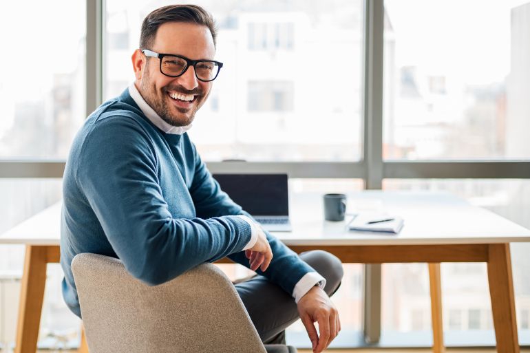 Portrait of young smiling happy handsome successful businessman entrepreneur freelancer working from home office or business office on laptop computer looking at camera.