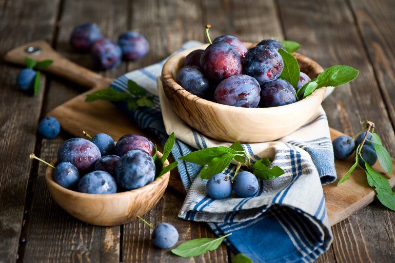 gettyimages-152007076-1762013653 Plums in wooden bowl with napkin.