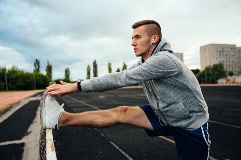 Close-up profile of a young handsome man doing exercises, working out legs, listening to music in headphones, dressed in sportswear, at the stadium أسباب تجعل التمرين الصباحي أقل فعالية المصدر: فري بيك