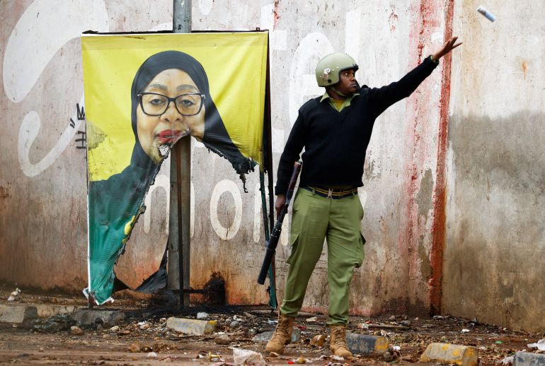 reuters_69053f9f-1761951647-2 A Tanzanian riot police officer throws a used teargas canister near a vandalised campaign poster of President Samia Suluhu Hassan, following a protest a day after a general election marred by violent demonstrations over the exclusion of two leading opposition candidates at the Namanga One-Post Border crossing point between Kenya and Tanzania, October 30, 2025. REUTERS/Thomas Mukoya