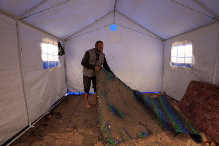 reuters_69197f97-1763278743 A Palestinian man lifts a muddied rug in a tent on a rainy day, during a ceasefire between Israel and Hamas, in Gaza City, November 14, 2025. REUTERS/Dawoud Abu Alkas
