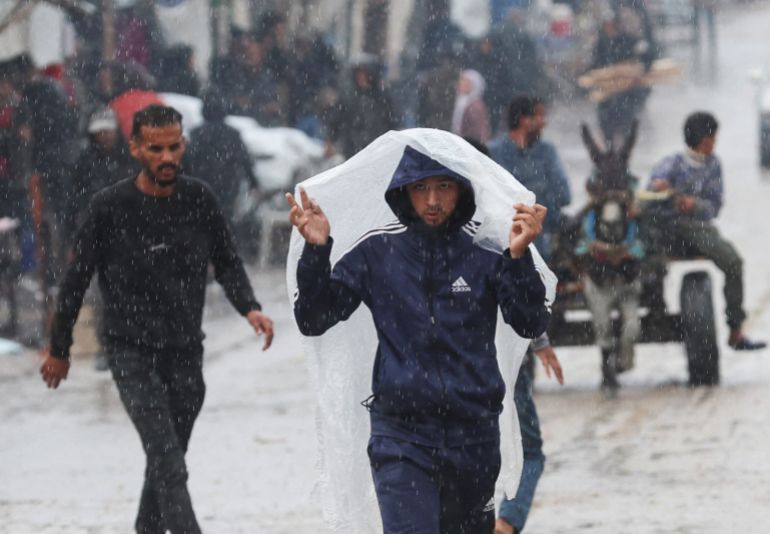 A Palestinian covers himself from the rain during a rainy day in Khan Younis in the southern Gaza Strip, November 25, 2025. REUTERS/Ramadan Abed