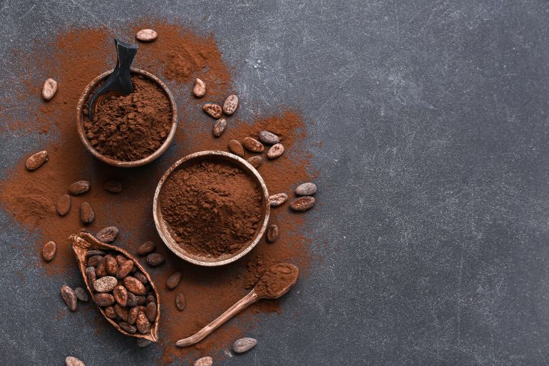 Bowls with cocoa powder and beans on black background