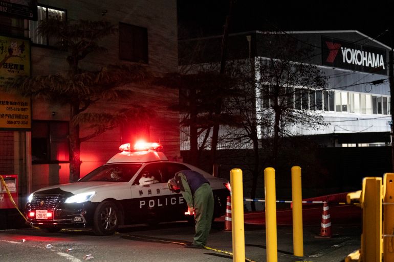 A worker bows as a police car leaves the Yokohama Rubber Mishima Plant in Mishima, Shizuoka Prefecture, on December 26, 2025. Fifteen people were injured in a stabbing attack in a rubber factory in central Japan on December 26, during which an unspecified liquid was also sprayed, emergency officials said. (Photo by Yuichi YAMAZAKI / AFP)