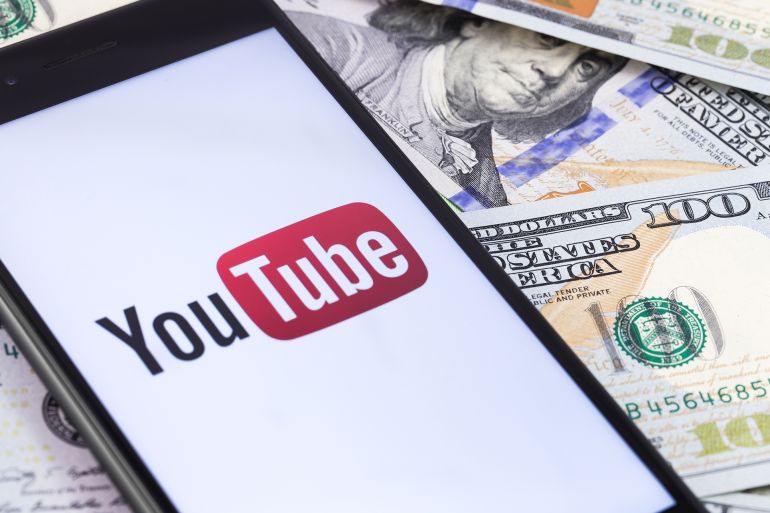 dollars banknotes and YouTube logo on the screen smartphone. YouTube is a free video sharing application that anyone can watch. Moscow, Russia - March 15, 2019