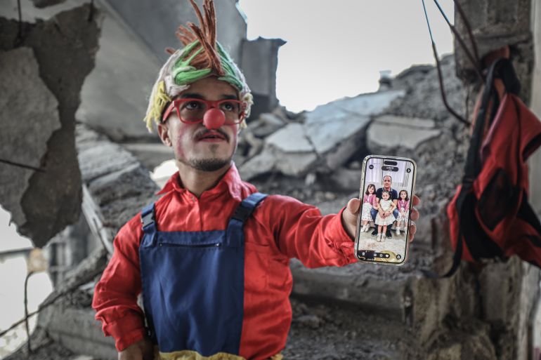 DEIR AL BALAH, GAZA - DECEMBER 13: Ahmed Mahmud Kamil Abu Seker, a 28-year-old resident of Bureij Refugee Camp who volunteers as a clown to make children laugh, shows the photos of his deceased relatives on his phone before meeting with the children in Deir al-Balah, Gaza on December 13, 2025. Despite losing his entire family in the war, Seker works as a clown to make children laugh, and despite all the difficulties, he tries to hold on to life in order to bring a smile to children's faces. ( Fadel A. A. Almaghari - Anadolu Agency )