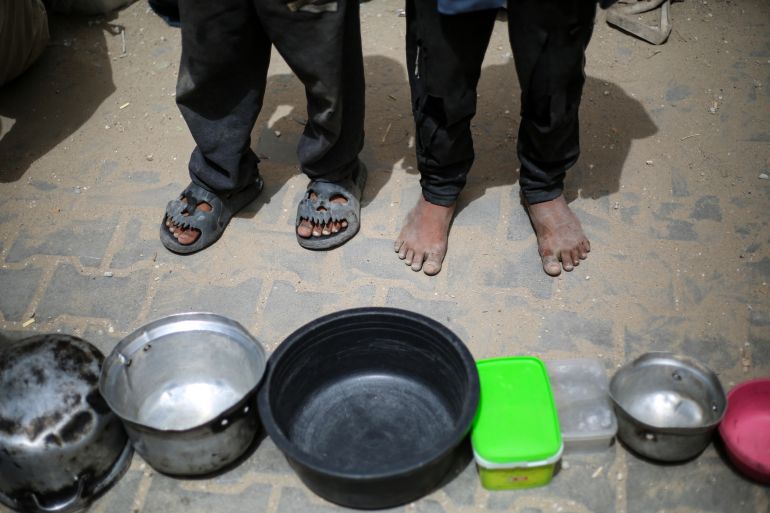 afp_682059b1d837-1746950577 TOPSHOT - Palestinian children stand over empty containers at a food distribution centre in the Nuseirat camp for refugees, in the central Gaza Strip, on April 30, 2025.