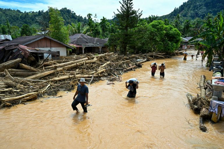 afp_692ee690eebb-1764681360-2 People wade through the floodwater in the aftermath of flash floods at Tukka village, Central Tapanuli, North Sumatra province, on December 2, 2025.