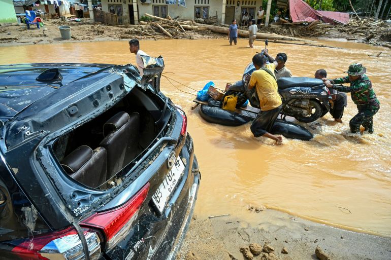 afp_692ff1c73c6a-1764749767 Villagers push a motorcycle on a makeshift raft along an inundated road in the aftermath of flash floods at Tukka village, Central Tapanuli, North Sumatra province, on December 2, 2025.