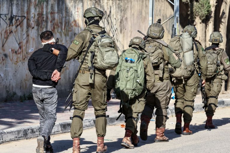 afp_6933b7f0ad72-1764997104-2 TOPSHOT - Israeli soldiers detain a Palestinian man during a military operation in the town of Qalqiya, in the occupied West Bank on December 4, 2025.