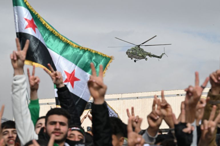 A chopper flies above people as they flash the victory sign while gathering to celebrate a year since the ousting of longtime ruler Bashar al-Assad in the Syrian capital Damascus on December 8, 2025.