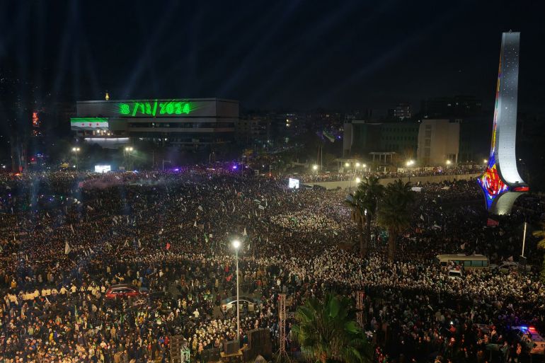 afp_6937e0d36242-1765269715 An aerial photograph shows thousands of people celebrating the first anniversary since the ousting of longtime ruler Bashar al-Assad near The Damascus Sword monument in Omayyad Square, in the Syrian capital Damascus on December 8, 2025.