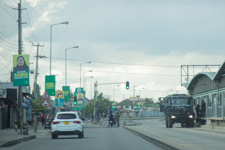afp_69383d2db025-1765293357 An electoral poster of Tanzania's President Samia Suluhu Hassan is seen as police officers inspect vehicles at a deserted intersection in Dar Es Salaam on December 9, 2025 during a day of demonstrations agaisnt the violent crackdown by security forces on election demonstrations. (Photo by AFP)