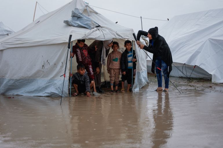 afp_693b31e1ecf4-1765487073-1 A woman fixes her tent as children stand inside at a makeshift camp sheltering displaced Palestinians after heavy rains in the Zeitoun neighbourhood of Gaza City on December 11, 2025.