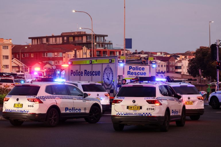 afp_693e8e952aa7-1765707413 Police vehicles are seen on a road after a shooting incident at Bondi Beach in Sydney on December 14, 2025.