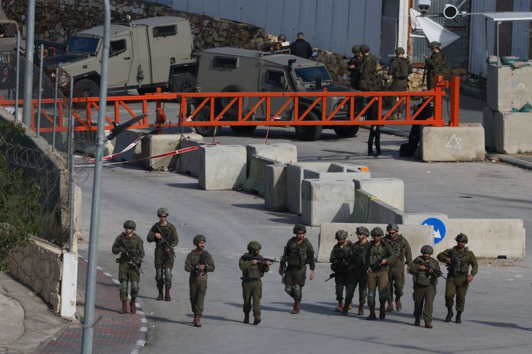 afp_693ee7983c0d-1765730200 Israeli security forces gather at the site where a Palestinian man was shot and killed at the north entrance of the occupied West Bank city of Hebron on December 14, 2025.