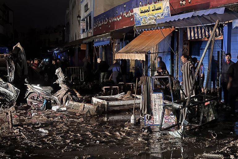 afp_693fb9f96969-1765784057 People walk past debris left by a flash flood in Safi on December 14, 2025.
