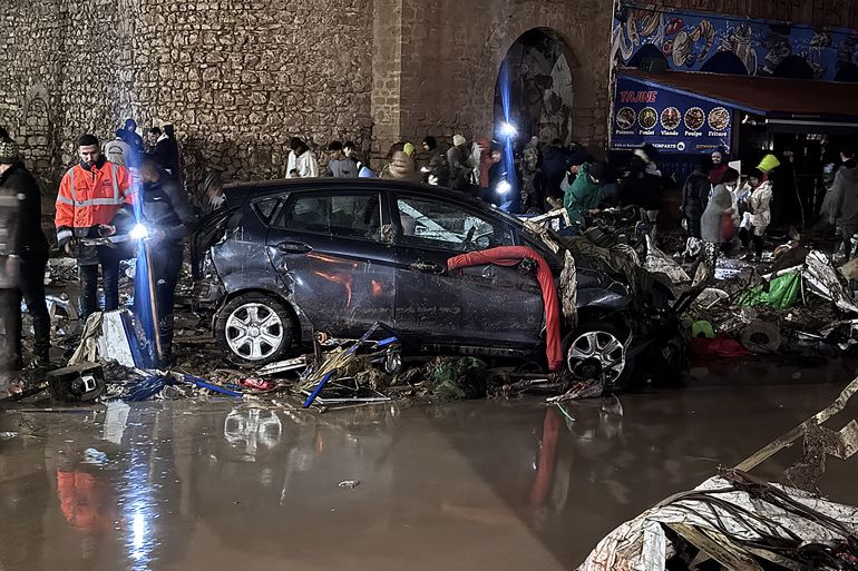 afp_693fba0dbb88-1765784077 People walk past debris left by a flash flood in Safi on December 14, 2025.