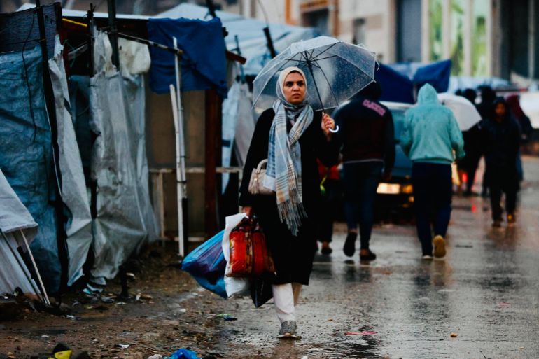 afp_694105eec425-1765869038 A displaced Palestinian woman holds an umbrella to shield from the rain in Gaza City on December 15, 2025.