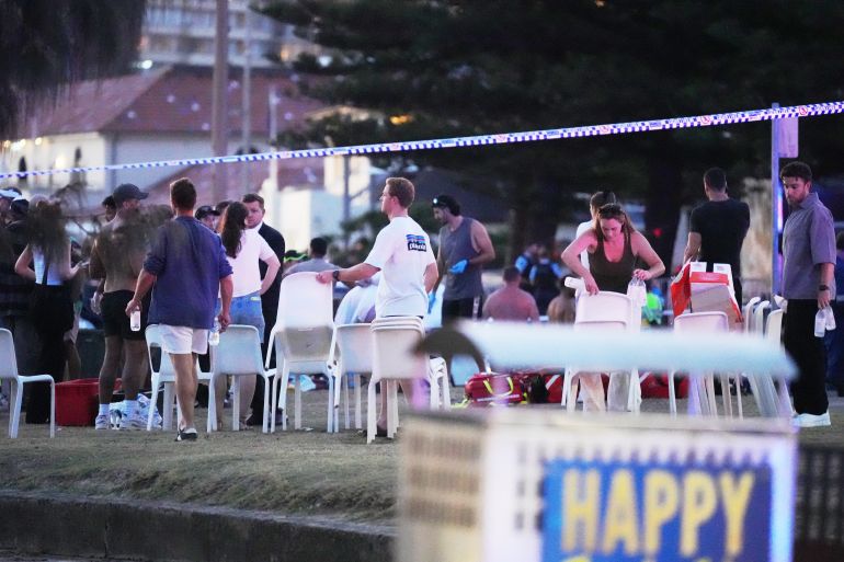 ap25348340433174-1765706317 People and emergency workers gather at location where a holiday event was taking place and then a reported shooting at Bondi Beach in Sydney, Sunday, Dec. 14, 2025. (AP Photo/Mark Baker)
