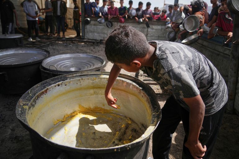 ap_682af2b8b8740-1747645112 A boy scrapes leftovers from an empty pot after all the meals were distributed at a community kitchen in Khan Younis, southern Gaza Strip, Wednesday, May 14, 2025. (AP Photo/Abdel Kareem Hana)