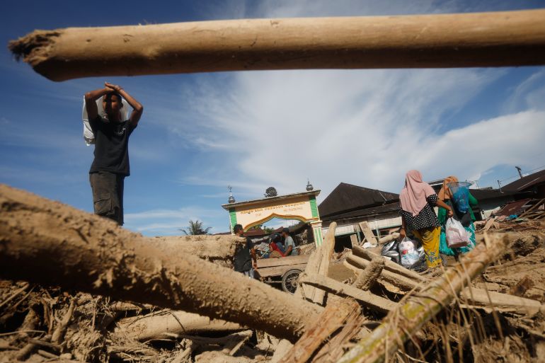 ap_692ff11a84ce0-1764749594 Survivors walk past logs swept away by a flash flood in Batang Toru, North Sumatra, Indonesia, Tuesday, Dec. 2, 2025. (AP Photo/Binsar Bakkara)