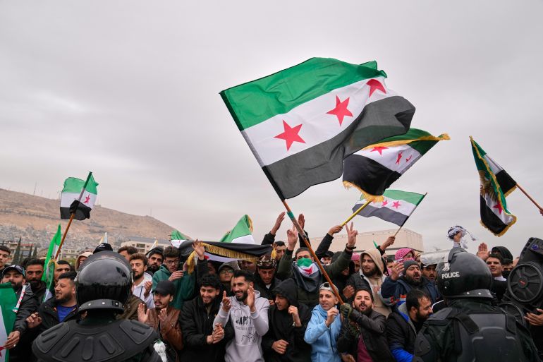 People celebrate and wave Syrian flags as they wait for a parade by the new Syrian army marking the first anniversary of the ousting of the Bashar Assad regime in Damascus, Syria, Monday, Dec. 8, 2025. (AP Photo/Hussein Malla)