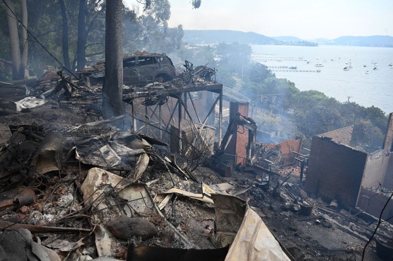 ap_69368d31321d7-1765182769 Ruins of buildings and a car smolder after a wildfire destroyed houses in Koolewong, Australia, Saturday, Dec. 6, 2025. (Dan Himbrechts/AAP Image via AP)