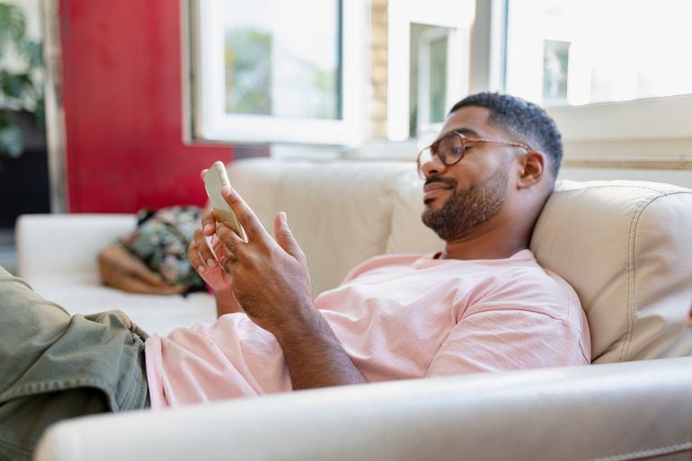 Relaxed man sitting on sofa using cell phone - stock photo