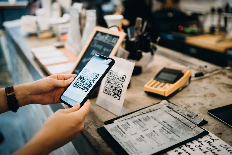 gettyimages-1177644546 Customer scanning QR code, making a quick and easy contactless payment with her smartphone in a cafe