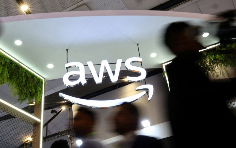 reuters_68f73f95-1761034133 FILE PHOTO: People walk past the logo of Amazon Web Services (AWS) at its exhibitor stall at the India Mobile Congress 2025 at Yashobhoomi, a convention and expo center in New Delhi, India, October 8, 2025. REUTERS/Anushree Fadnavis/File Photo