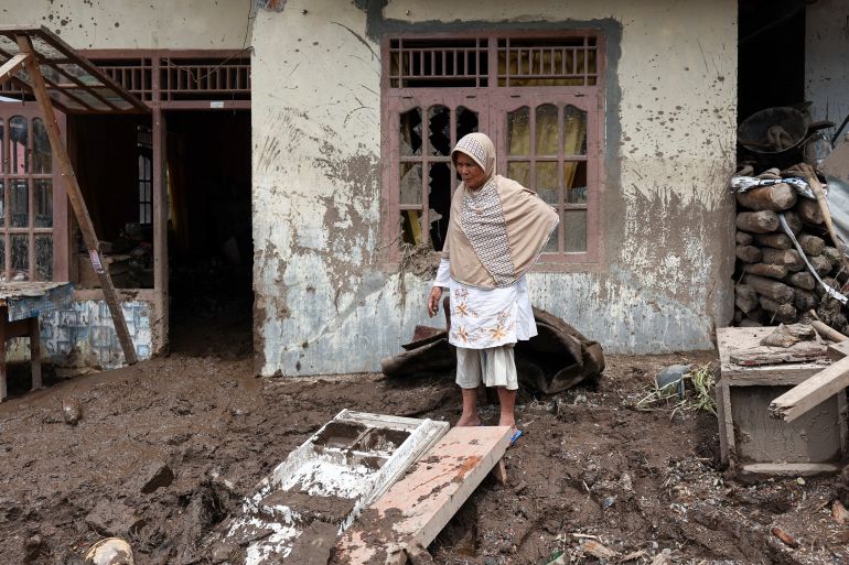 reuters_692ff100-1764749568 Nur Hasanah, 71, stands in front of her house after deadly landslides following heavy rains in Malalak, Agam regency, West Sumatra province, Indonesia, December 3, 2025. REUTERS/Willy Kurniawan