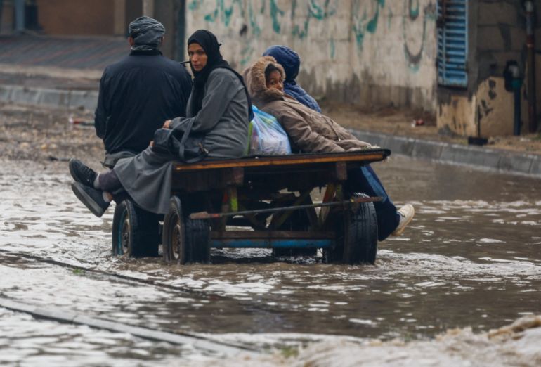 reuters_693c7513-1765569811 Displaced Palestinians make their way through a flooded street on a cart, during a rainy day in Nuseirat, central Gaza Strip, December 11, 2025. REUTERS/Mahmoud Issa