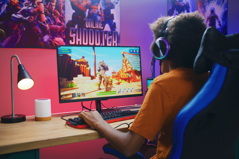 Professional eSports African American young gamer puts on headphones and plays online third-person 3D shooter on modern PC in stylish neon room. Video game live streaming or cybersport competition.