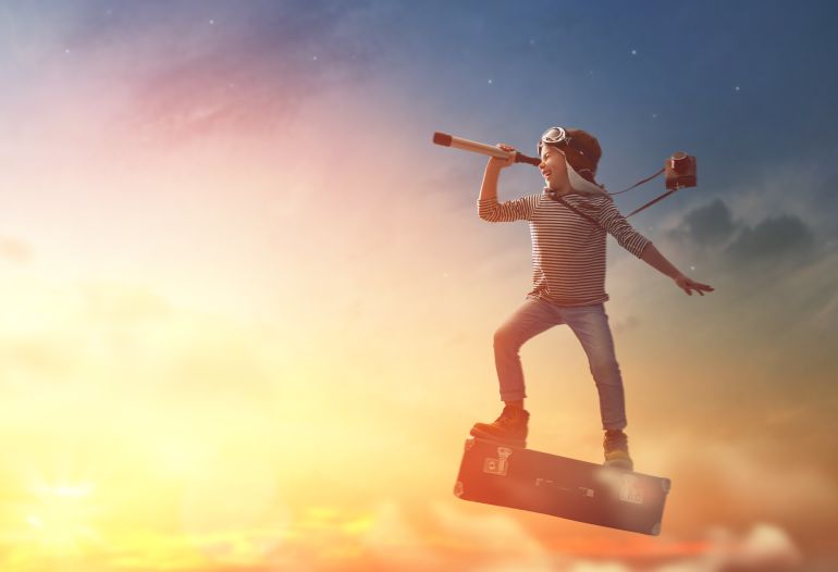 Dreams of travel! Child flying on a suitcase against the backdrop of sunset.