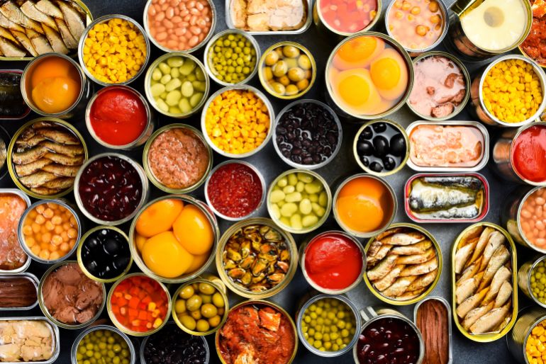 A large set of pickled and canned foods on the background. Metal cans with canned vegetables, beans, fish, seafood and fruit. Top view.