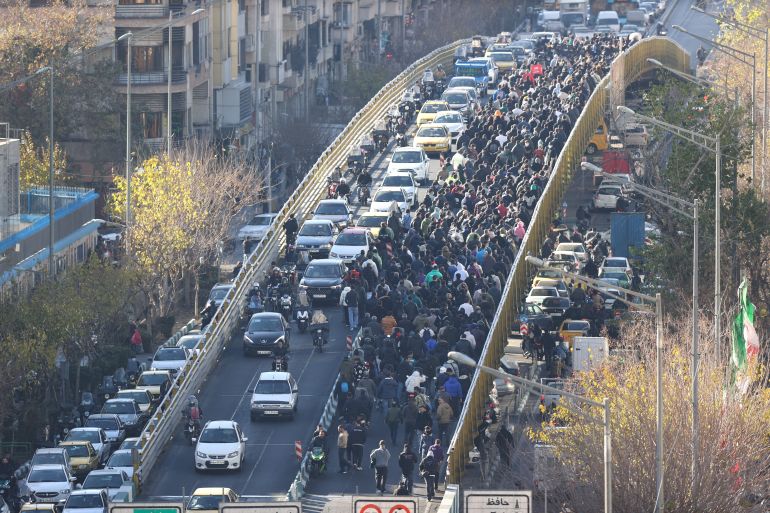 afp_69568ffc70cd-1767280636-3 Shopkeepers and traders walk over a bridge during a protest against the economic conditions and Iran's embattled currency in Tehran on December 29, 2025.
