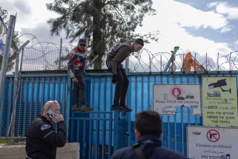 People standing on a fence look at heavy machinery demolishing a structure inside the headquarters of the United Nations Relief and Works Agency (UNRWA) in the Sheikh Jarrah neighbourhood of Israeli-annexed east Jerusalem on January 20, 2026.