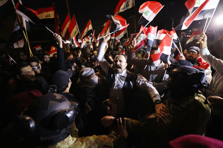 Iraqis raise their flags during a protest at the entrance to the Hanging Bridge, one of the entrances to the Green Zone in Baghdad on January 28, 2026.
