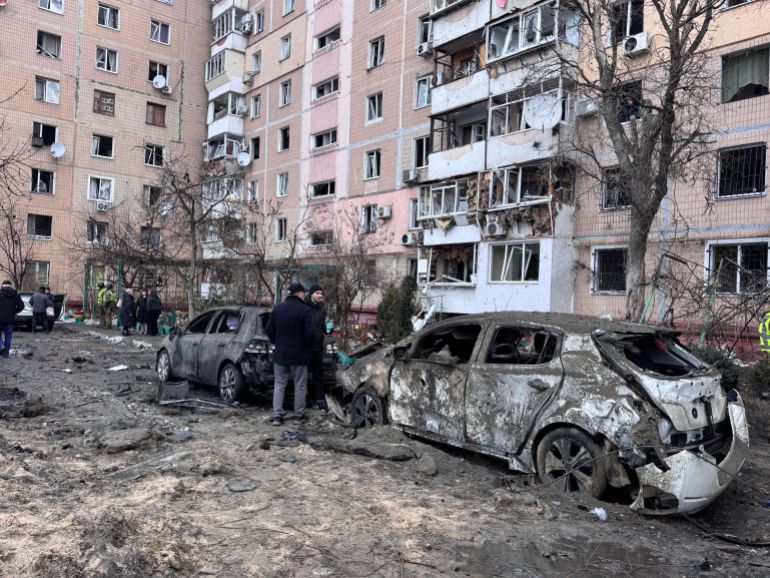 afp_697b9fae0694-1769709486 People stand next to burned cars and a damaged residential building in an area hit by an air attack in a residential neighborhood in Zaporizhzhia on January 28, 2026, amid the Russian invasion of Ukraine. (Photo by Darya NAZAROVA / AFP)