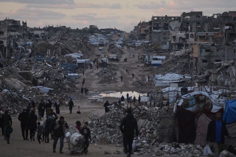 Palestinians walk past destroyed buildings in the northern Gaza Strip, Friday, Jan. 2, 2026. (AP Photo/Jehad Alshrafi)