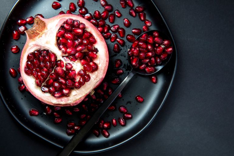Pomegranate half placed on a plate with the seeds spread on plate.