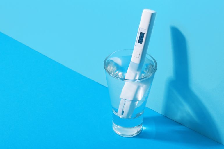 digital tester to determine water quality control and lowers it into a glass of drinking water for analysis, at home, close-up.