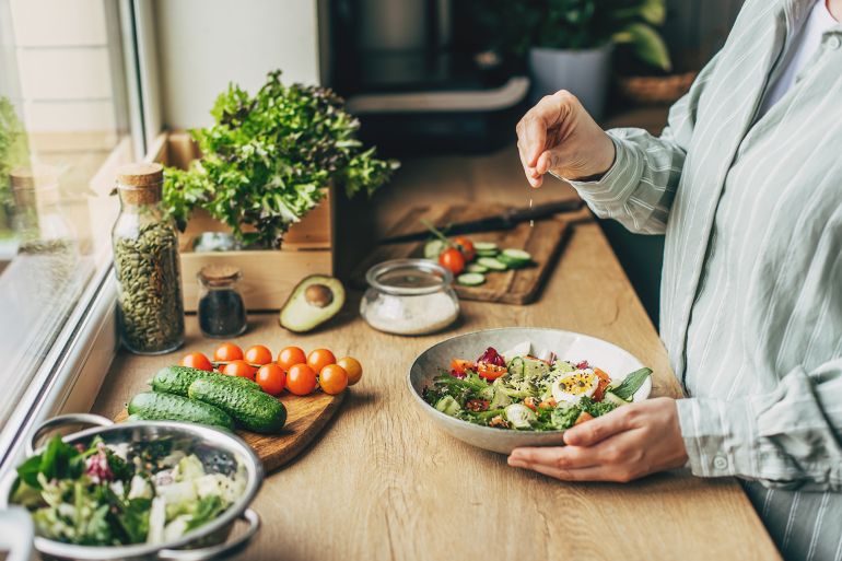 Woman mixing delicious superfood salad ingredients with wooden spoons in kitchen