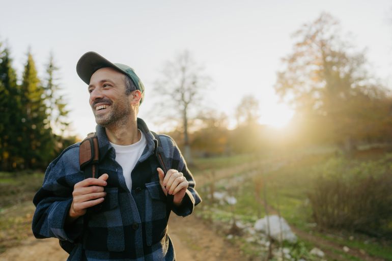 Photo of a mid adult man having a walk with a backpack through beautiful nature on a beautiful autumn day