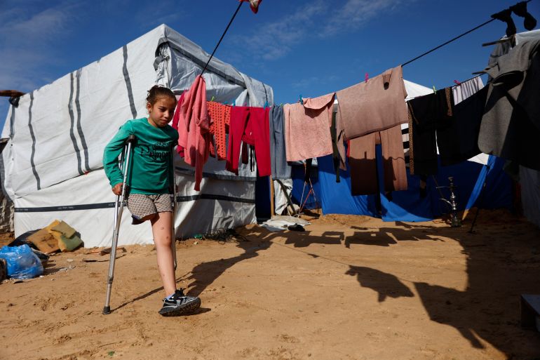 Ten-year-old Malak Khader, who lost her right leg, and who is the sole survivor of her family after all her relatives were killed in the Israeli army bombing of the Fatima Bint Assad School, in Jabalia in May 2025, walks towards her grandmother, Naifa Khader, 72-years-old, whom she now lives with, in a camp for displaced people in Jabalia, northern Gaza Strip on January 17, 2026. The majority of Gaza's 2.4 million people have been displaced, often multiple tim es, by the war that began with Hamas's attack on southern Israel on October 7, 2023. With displaced families living in tented camps, a serious concerns has been raised over their living conditions. (Photo by Omar AL-QATTAA / AFP)