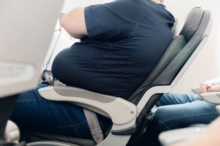 Fat obese man passenger fastening seat belt on airplane, problem safe flight.