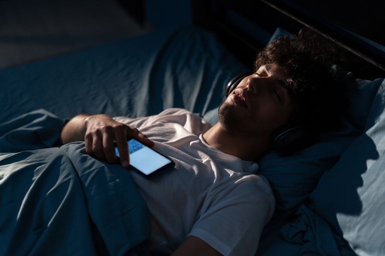 Young arabic man listening to music while resting in bed at home at night. Copy space; Shutterstock ID 2316488449; purchase_order: aj; job: ; client: ; other: