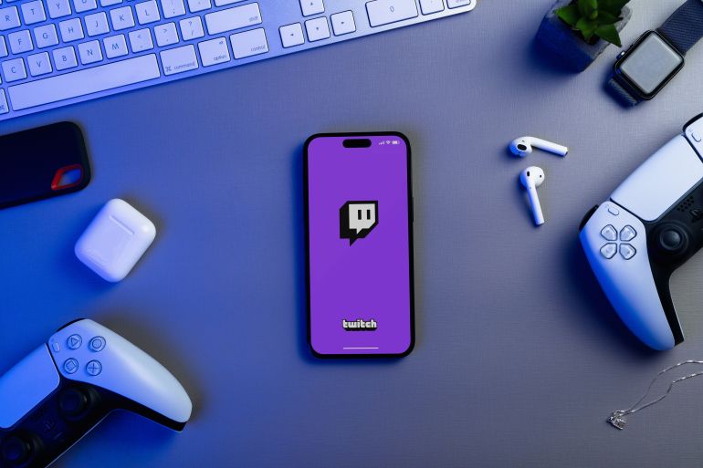 Twitch app on the smartphone iPhone 14 Pro screen with PS5 video game controllers. Top view. Office environment. Low blue light. Rio de Janeiro, RJ, Brazil. June 23 2023.